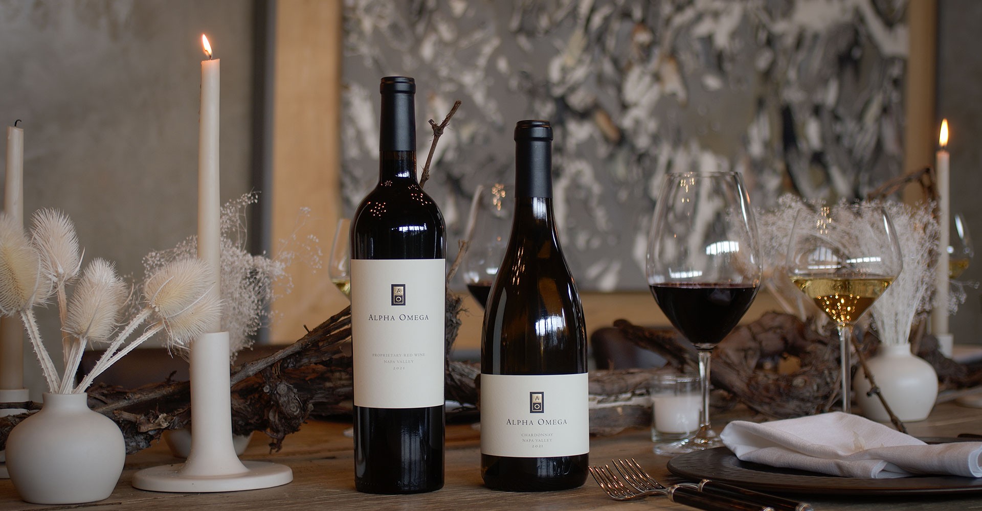 Two bottles of Alpha Omega wine on a table with candles and wine glasses